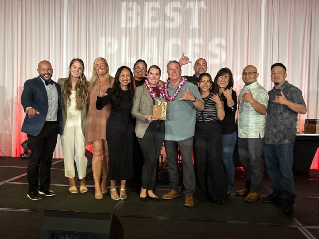 A group of men and women posing with a "Best Places to Work" plaque in front of a "Best Places to Work" stage curtain.
